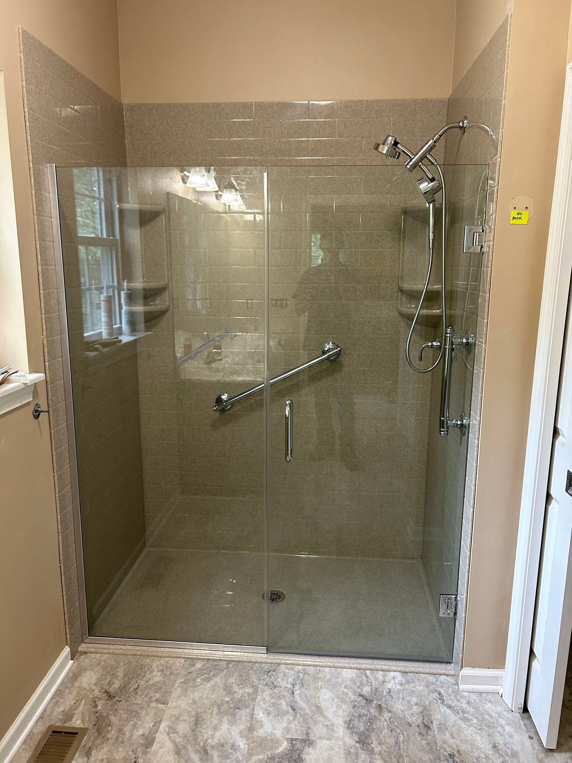 Glass shower enclosure with grab bar and multiple showerheads; tile walls and floor.