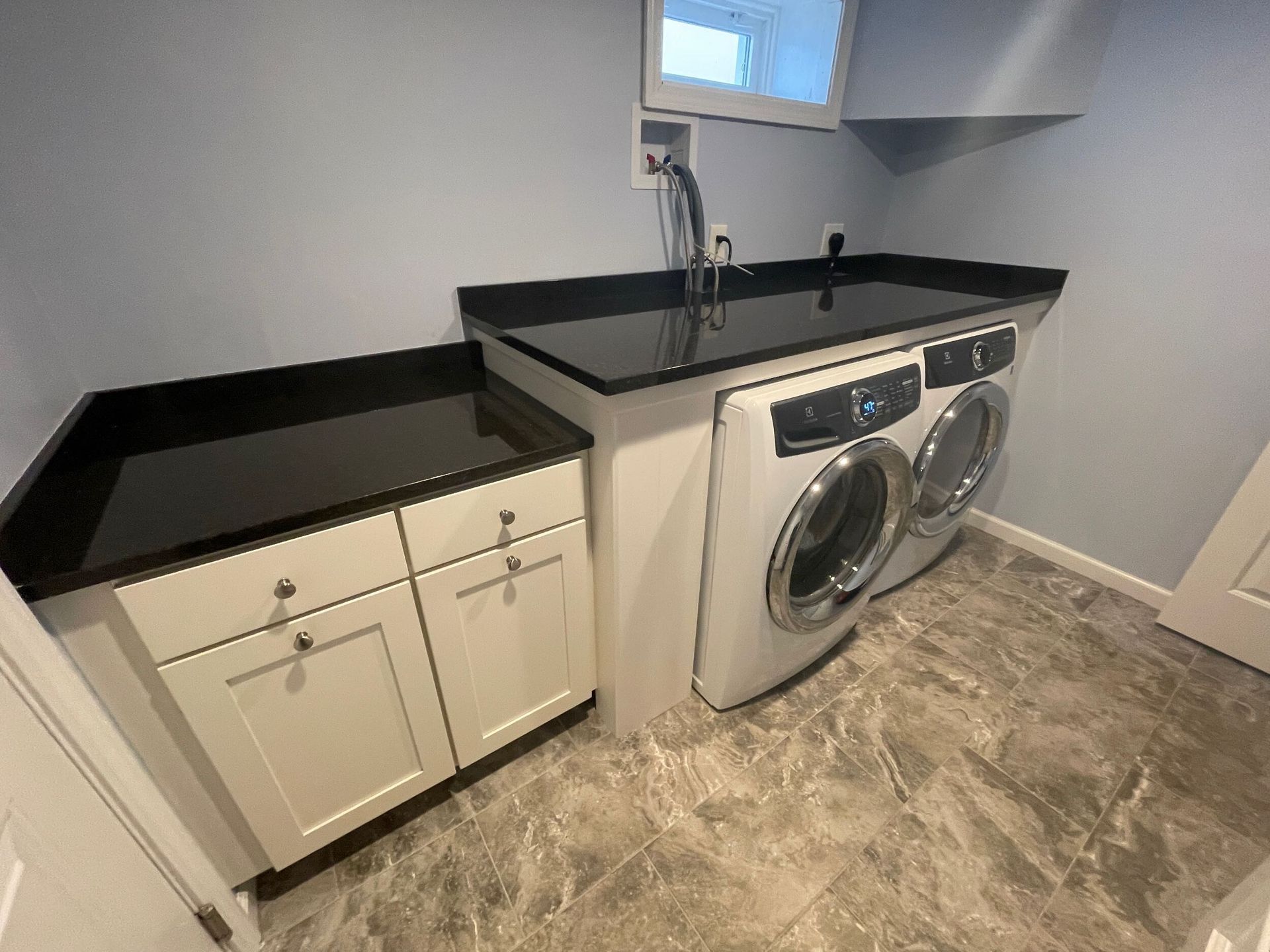 Laundry room with black countertop, white cabinets, washer/dryer, and a sink.