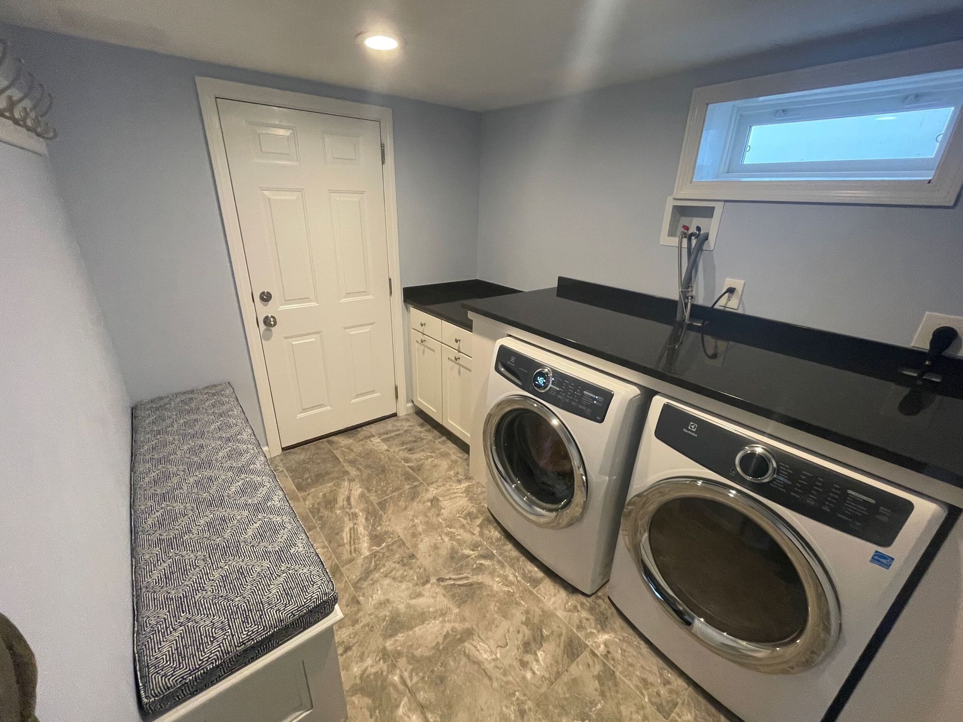 Laundry room with washer, dryer, countertop, bench, and window. Light blue walls, gray flooring.