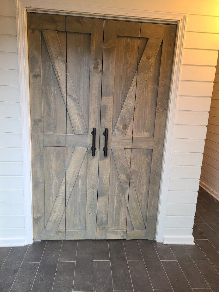 Wooden double doors with black handles and an X design, painted a gray-brown color.