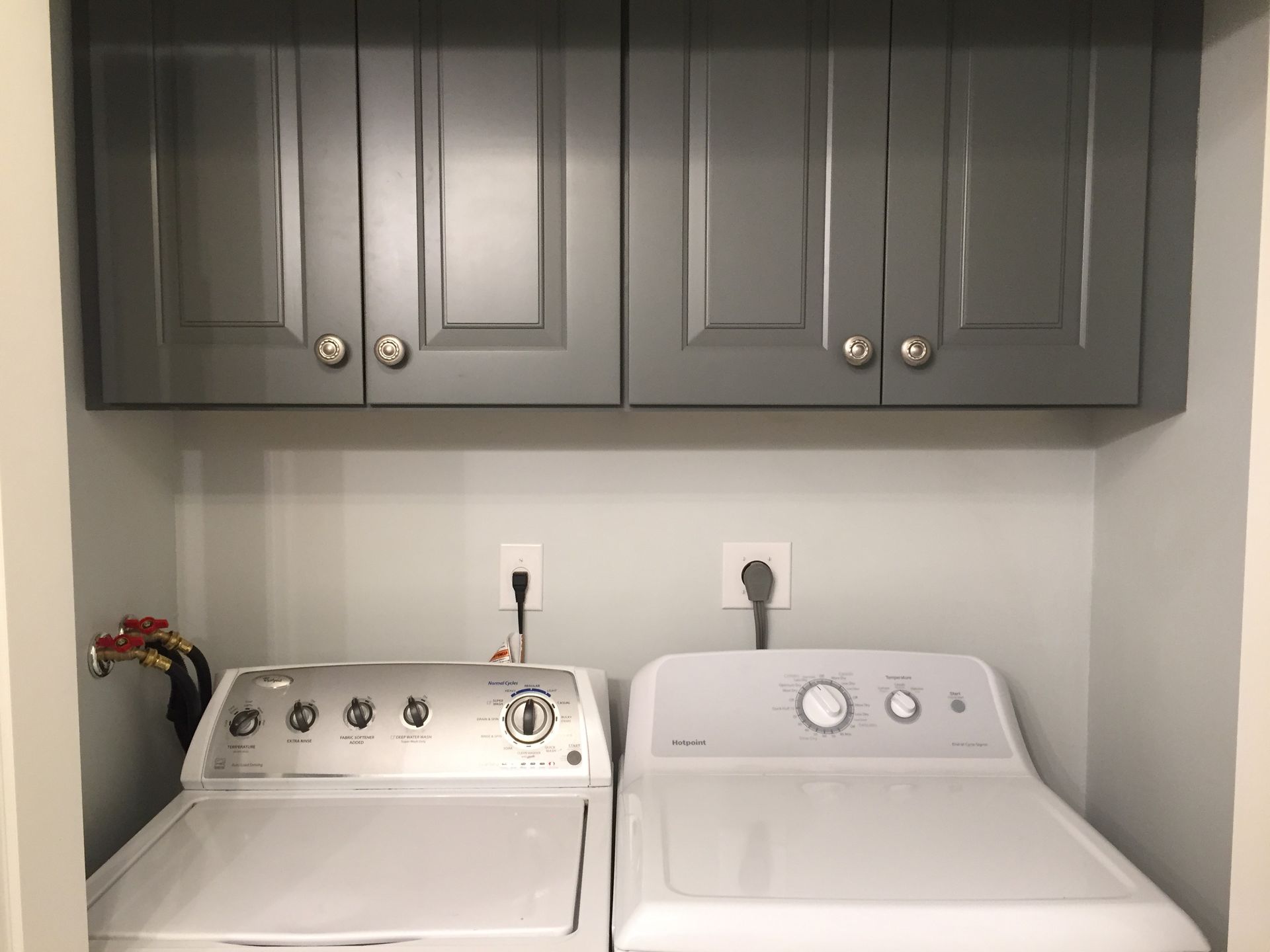Laundry room with a washing machine and dryer below grey cabinets.