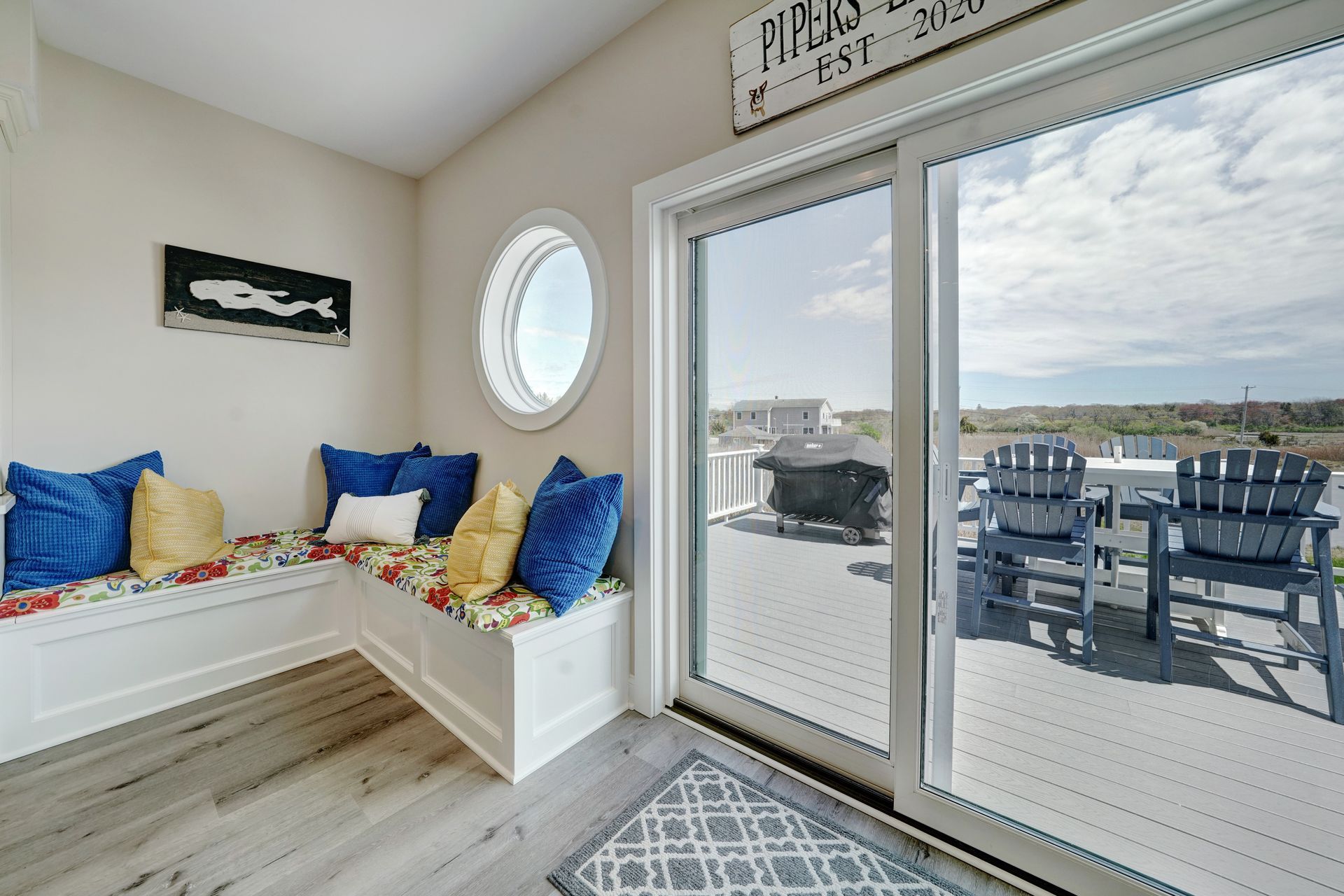 Coastal-themed room with a bench seat, porthole window, and sliding door to a deck with outdoor furniture.