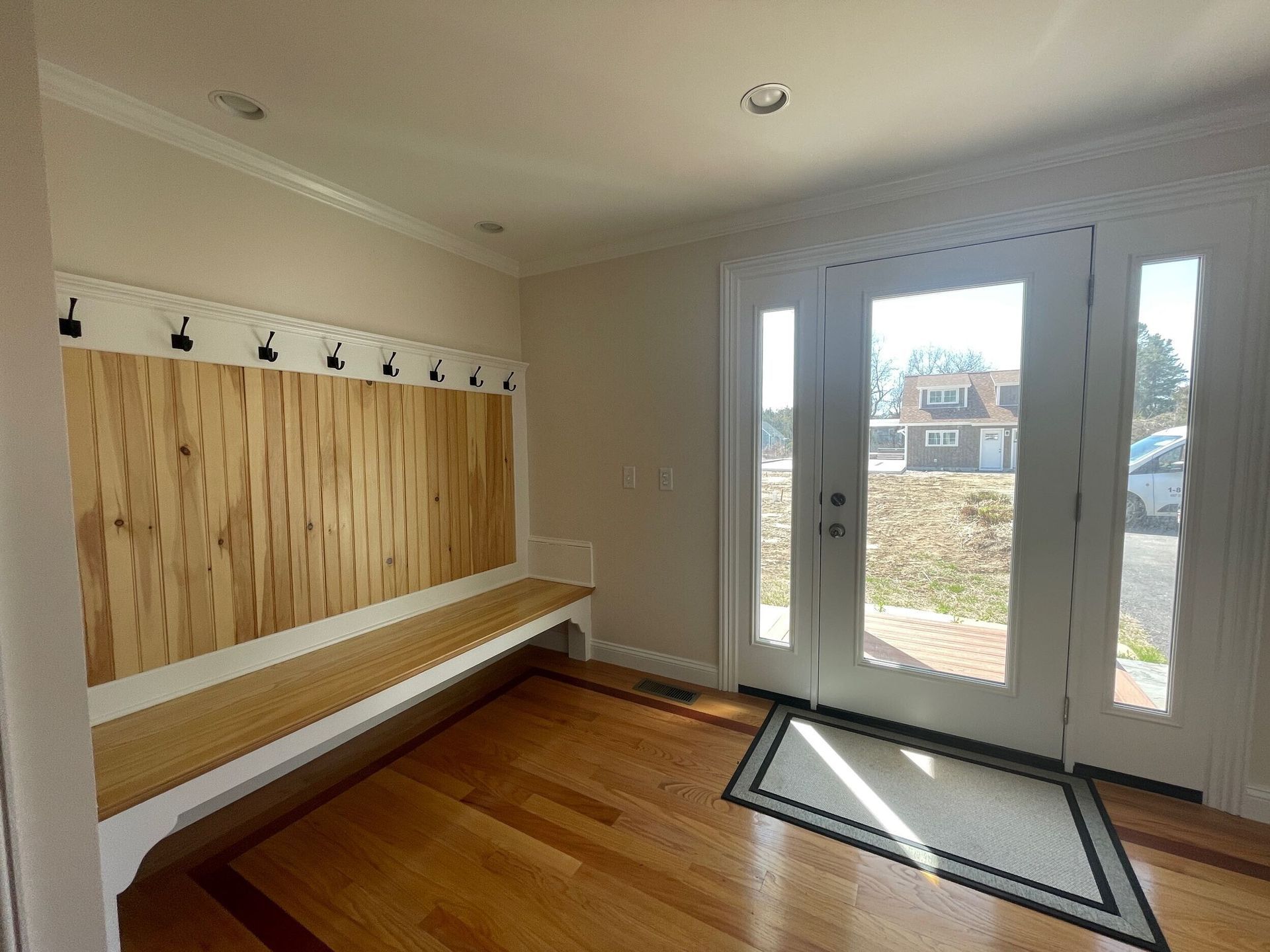 Entryway with wooden bench, coat hooks, and double glass doors.