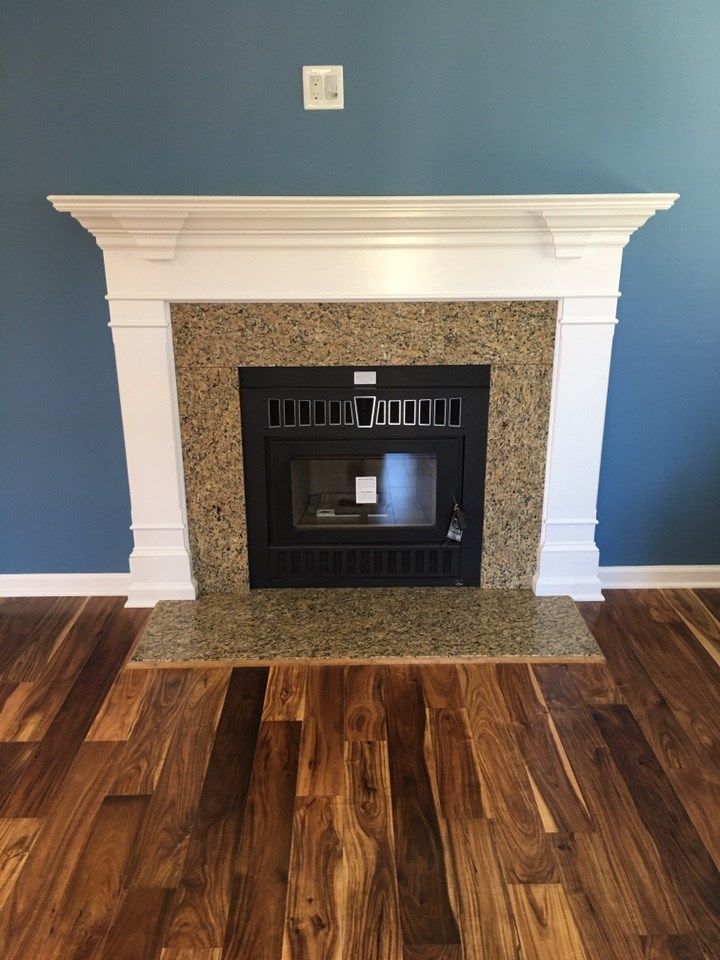 Fireplace with white mantel, speckled surround, black insert, and wood floor against blue wall.