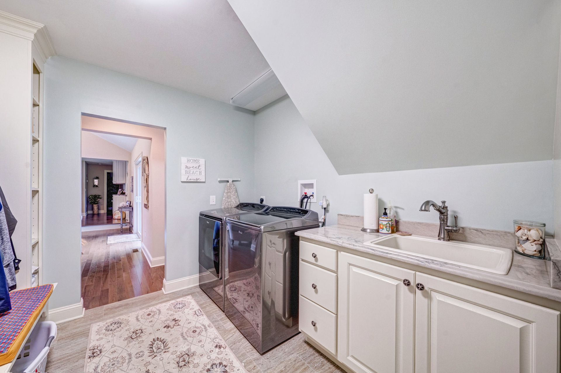 Laundry room with washer, dryer, sink, cabinets, light blue walls, and doorway to another room.