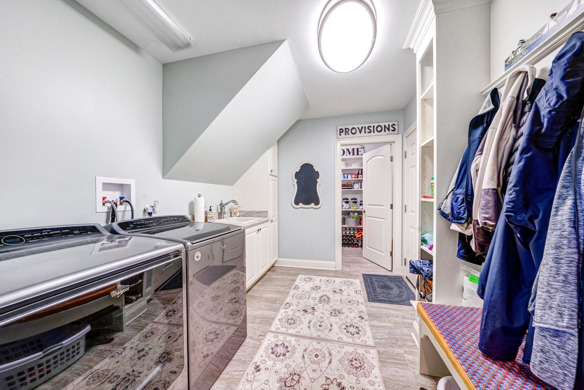 Laundry room with washer, dryer, sink, storage shelves, and coats hanging on a rack.
