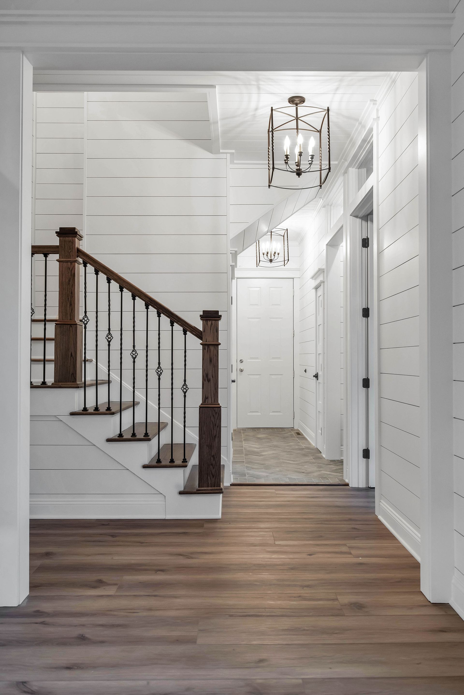 Hallway with stairs and wood flooring, shiplap walls, and decorative light fixtures.