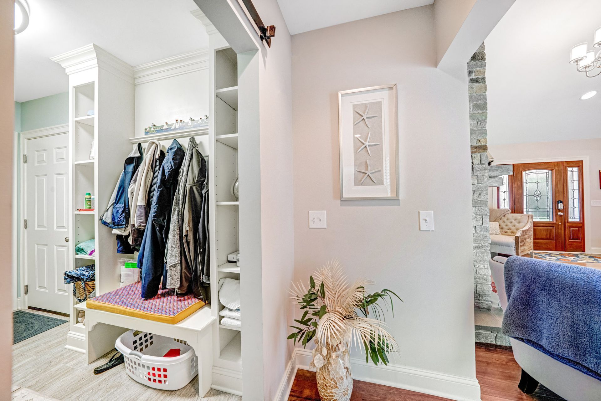 Hallway with built-in coat rack, shelves, bench, and sliding barn door. Light gray walls, hardwood floors, and decor.