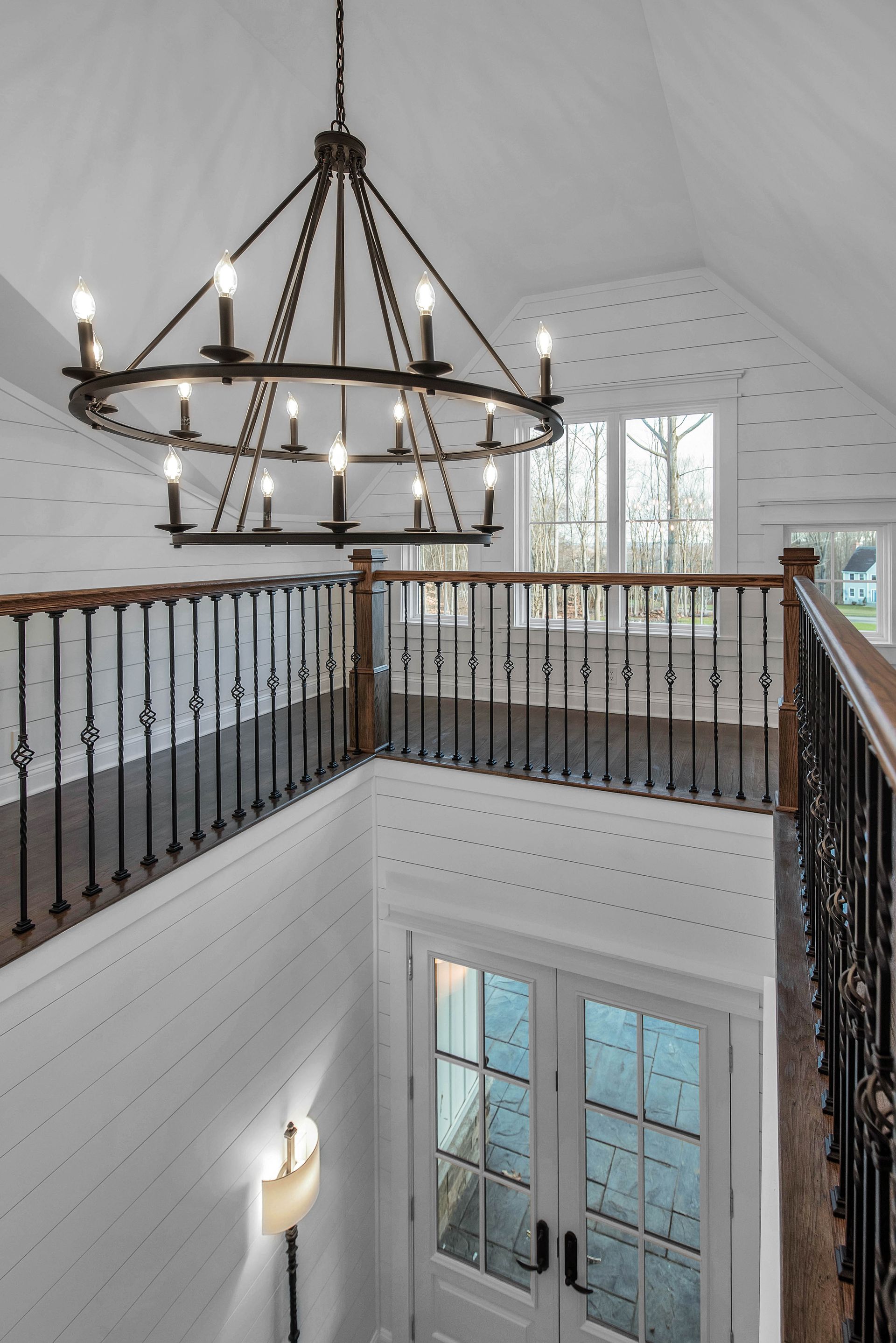 High-angle view of a two-story foyer with a chandelier, railing, and double doors. White walls with dotted pattern.