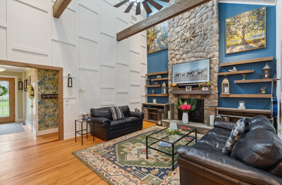 Living room with stone fireplace, blue accent wall, black leather sofas, and wood beams.