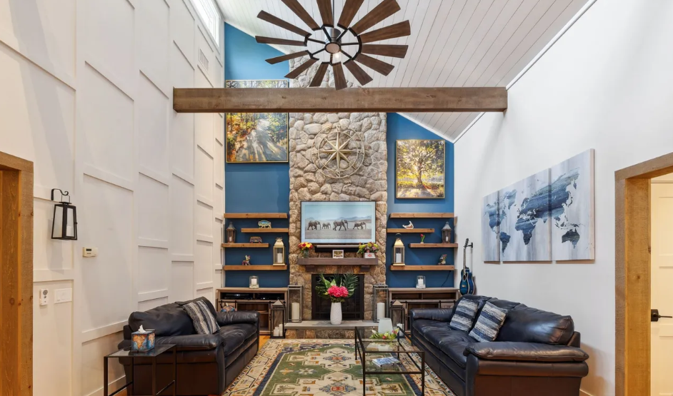 Living room with vaulted ceiling, stone fireplace, leather sofas, and a large wooden ceiling fan.