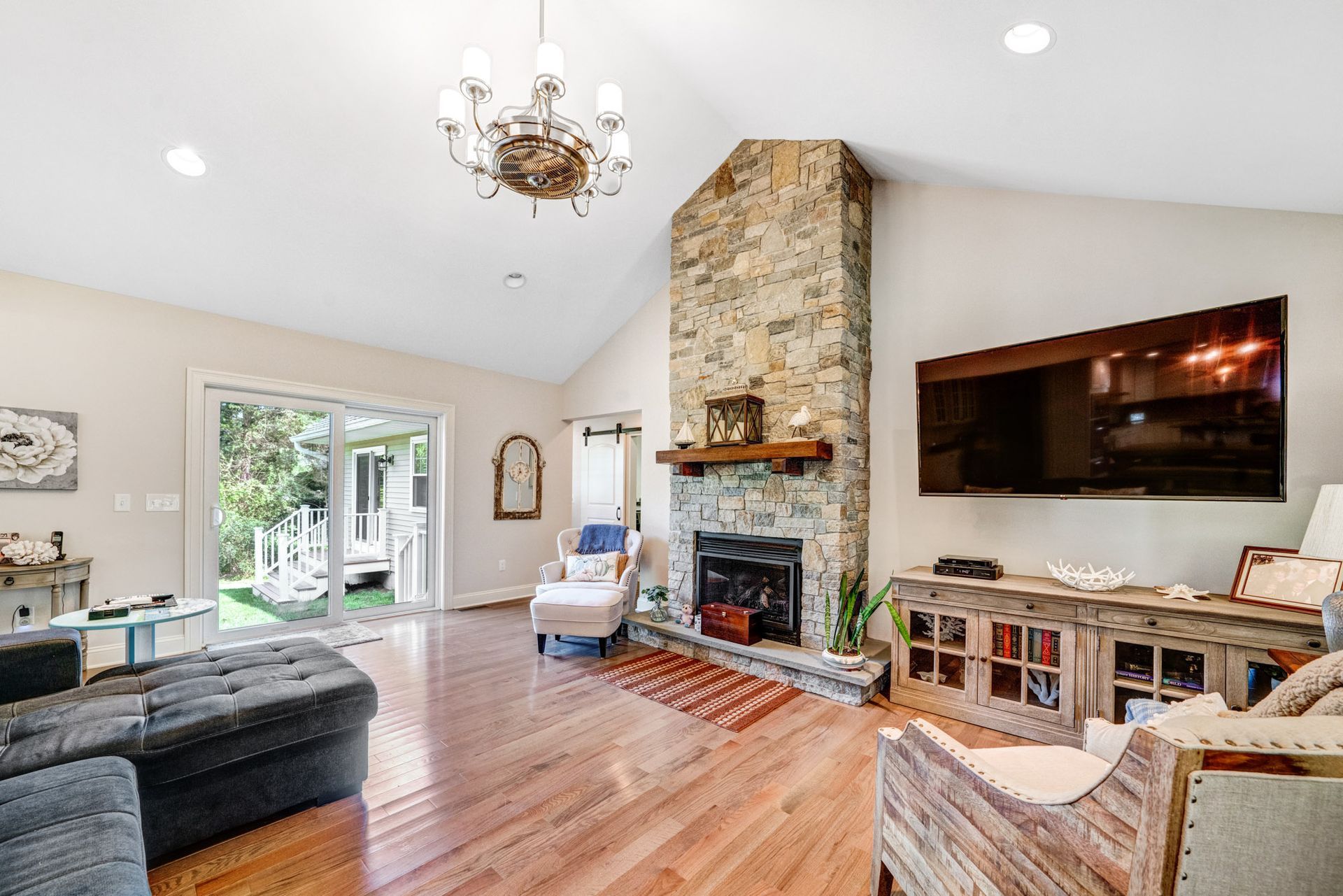 Living room with a stone fireplace, TV, wooden floors, and a sliding glass door to a deck.
