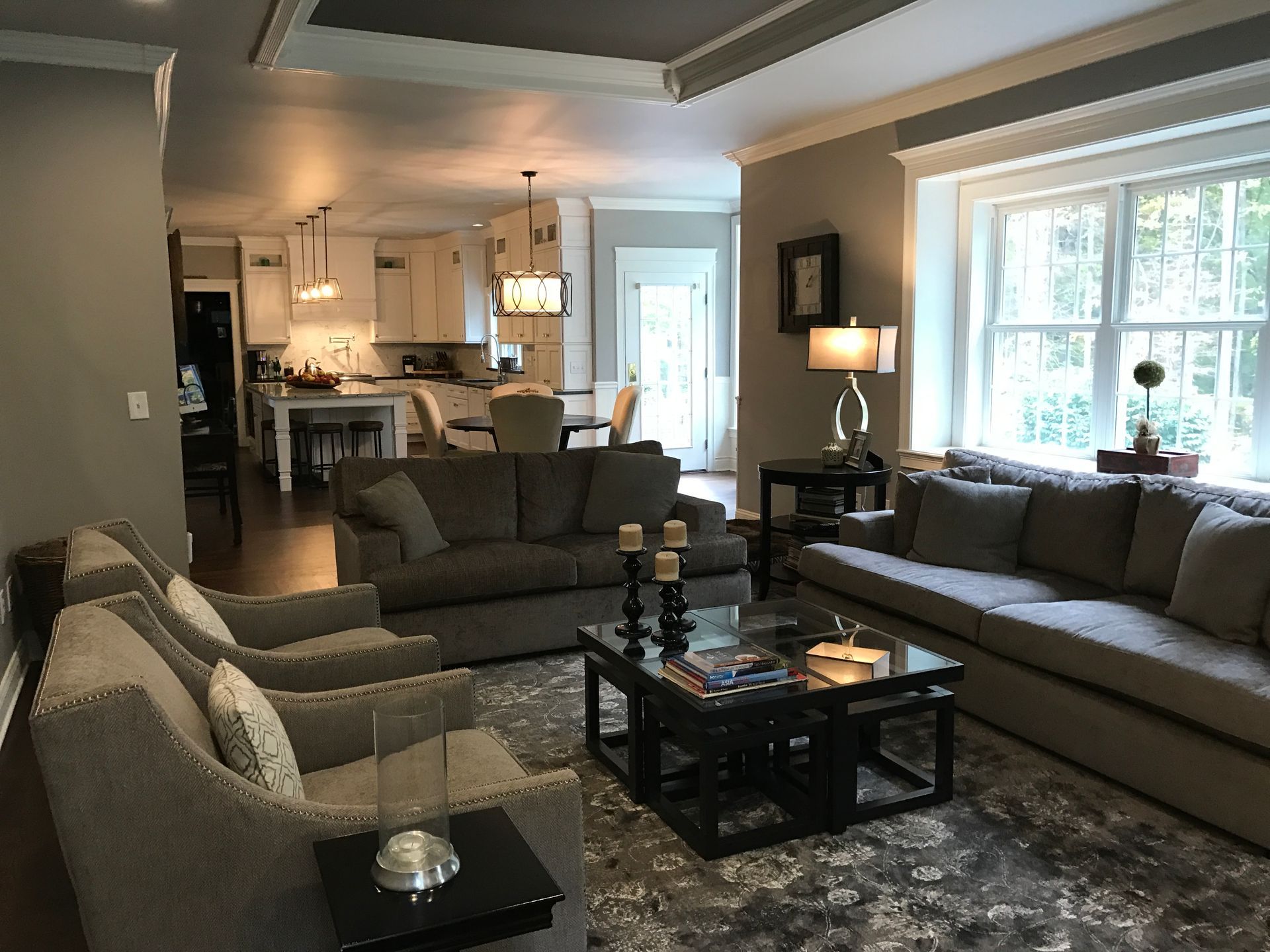 Living room with gray sofas, armchairs, coffee table, and open view to kitchen.