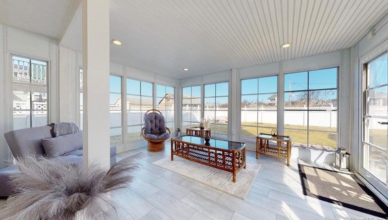 Sunroom with large windows, gray couch, wooden furniture, and light-colored floor. Bright and airy.