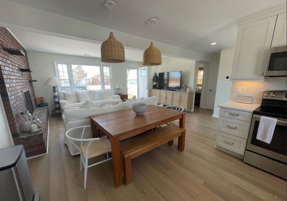 Open concept living area with kitchen, dining, and living room. Wooden table, white couch, brick wall, and woven light fixtures.
