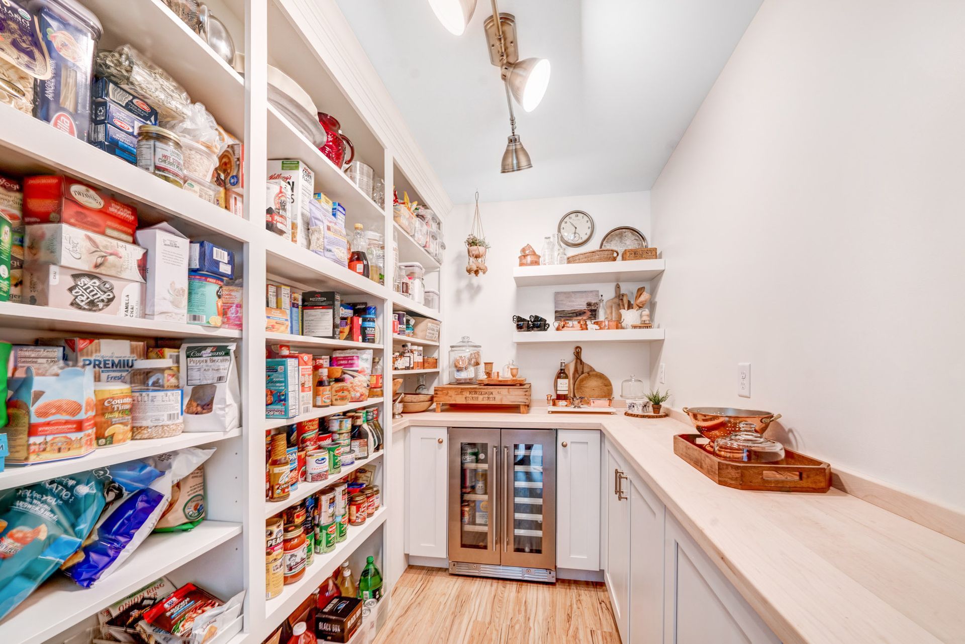 Well-stocked pantry with white shelves, various food items, counter space, and a wine cooler.