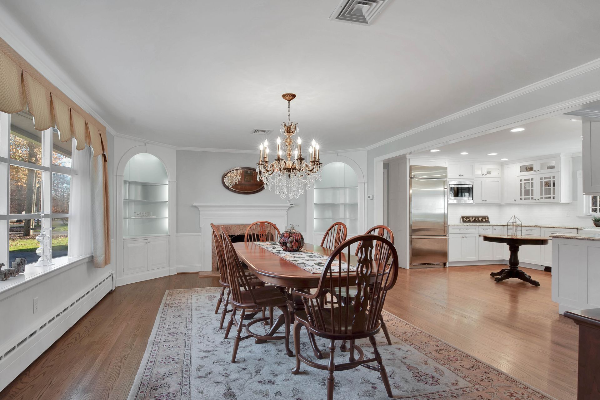 Dining room with wooden table, chairs, chandelier, and a view into a white kitchen.