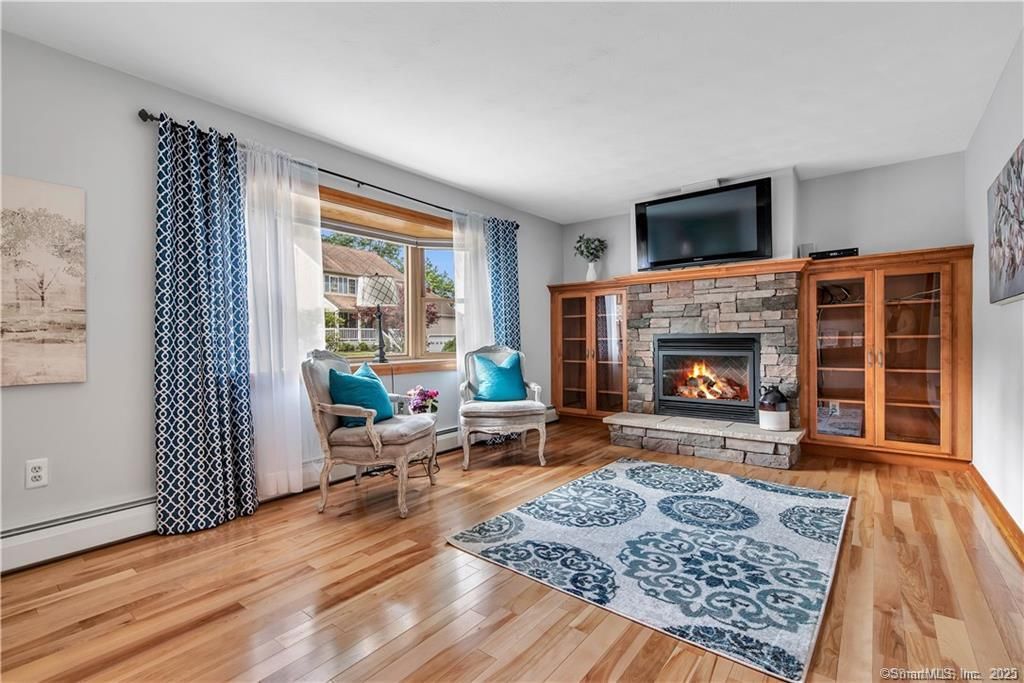 Living room with fireplace, TV, and blue and white decor. Hardwood floors and natural light.