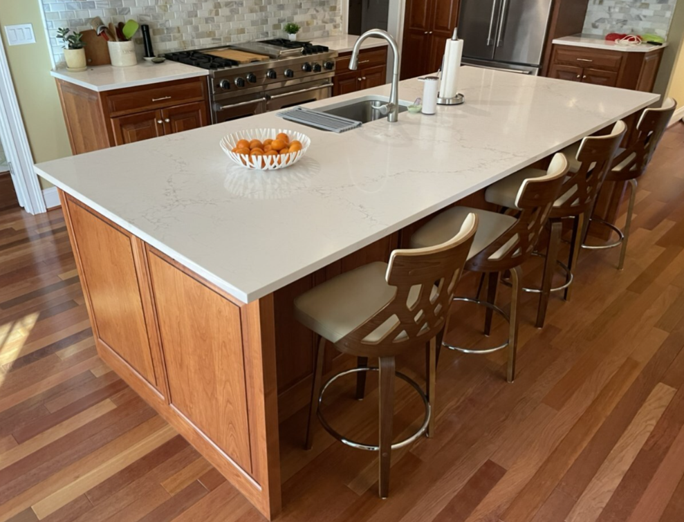 Kitchen island with seating, sink, and countertop. Wooden cabinets and flooring.