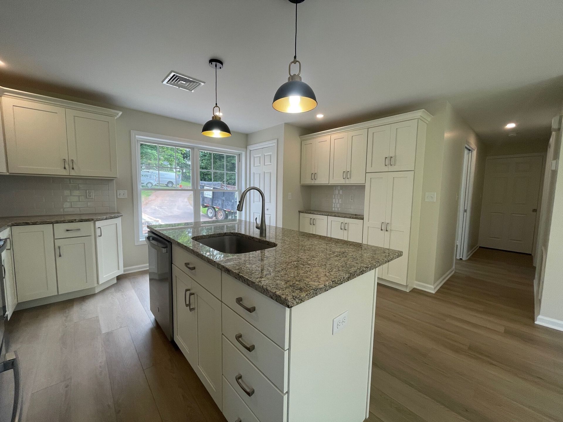 Kitchen with white cabinets, island with sink, granite countertops, pendant lights, and wood floors.