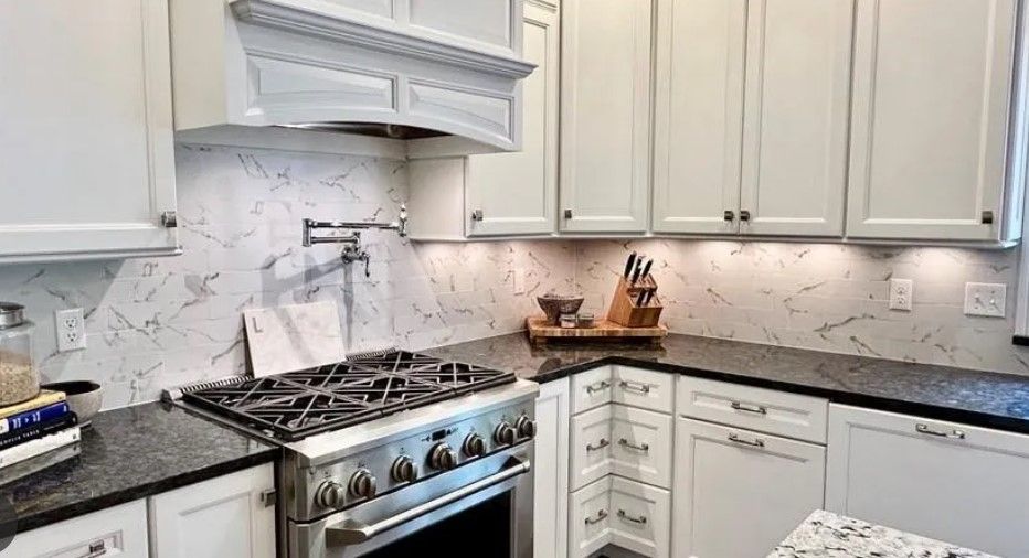 White kitchen with dark countertops, stainless steel stove, and white cabinets.