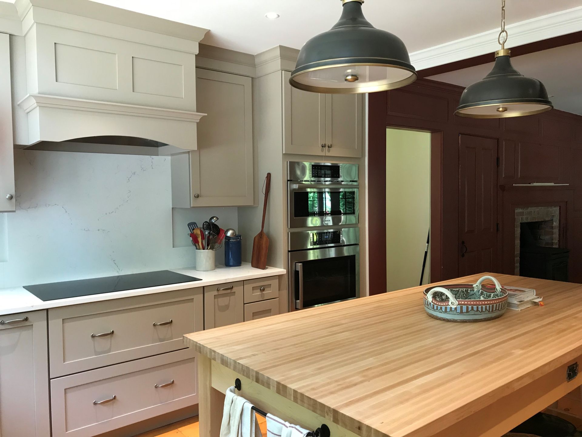 Kitchen with light gray cabinets, wood island, two pendant lights, and red-painted wall.