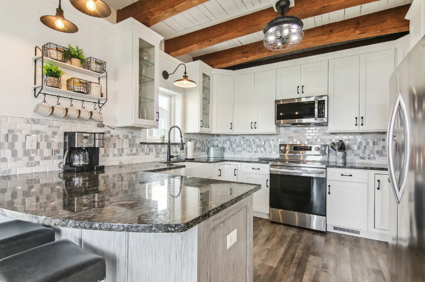 Kitchen with white cabinets, island with dark countertop, stainless steel appliances.
