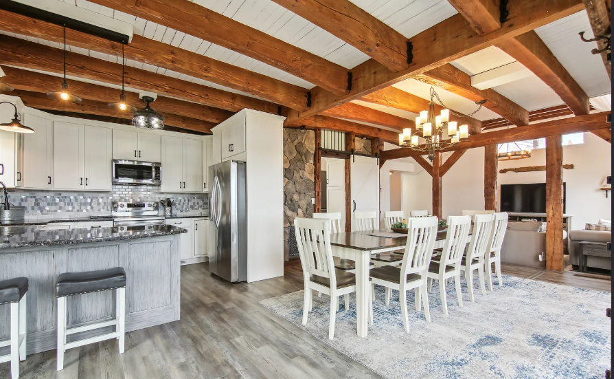 Kitchen and dining area with wood beams, white cabinets, granite countertops, and a large dining table.