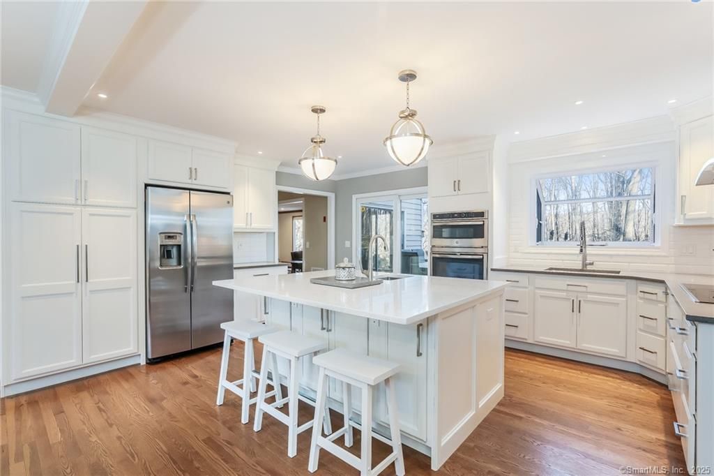 White kitchen with island, stainless steel appliances, and hardwood floors.
