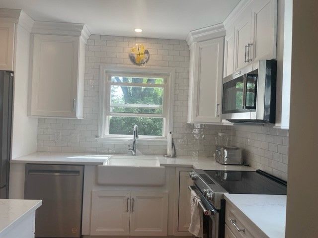 White kitchen with stainless steel appliances, white cabinets, and subway tile backsplash.