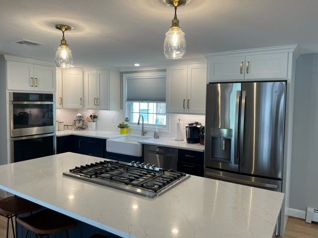 Modern kitchen with white and navy cabinets, stainless steel appliances, and a large island.