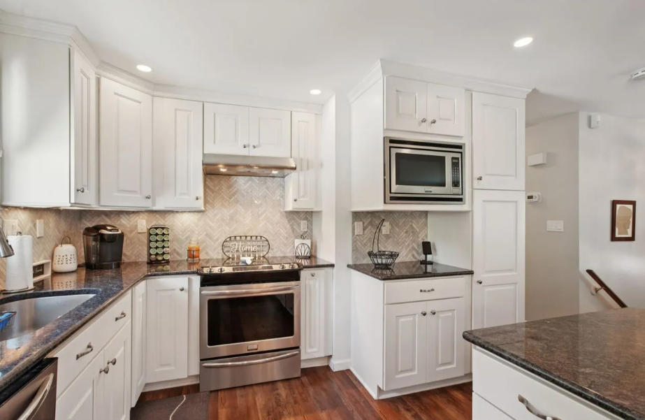 White kitchen with dark countertops, stainless steel appliances, and wood floors.