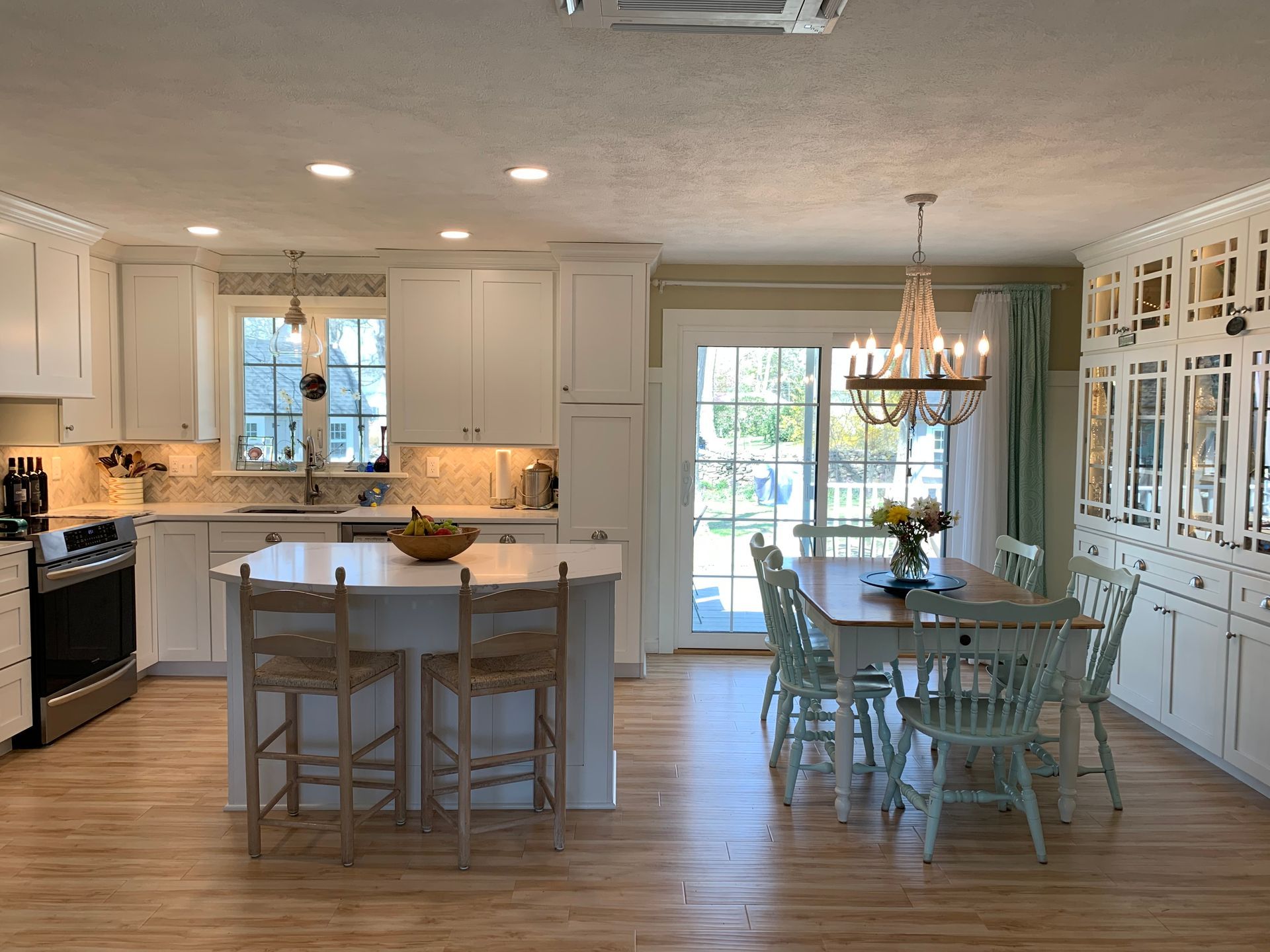 Bright kitchen with white cabinets, island with stools, dining table, and light wood floors.
