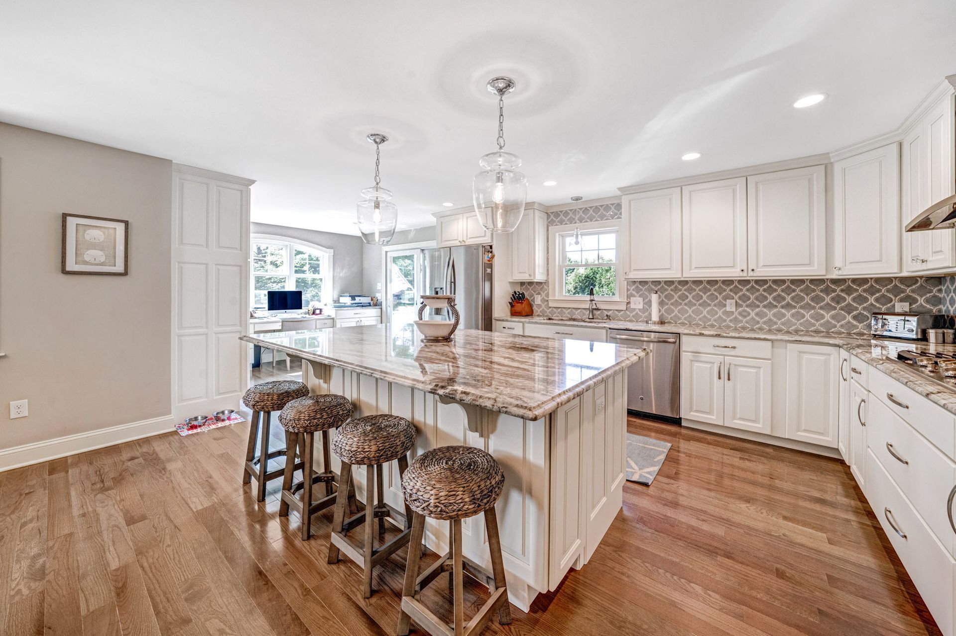 Bright kitchen with white cabinets, large island, wood floor, and stools.