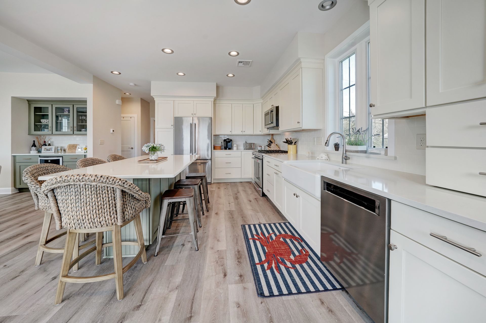 Bright, coastal kitchen with a large island, white cabinets, stainless steel appliances, and wood-look flooring.