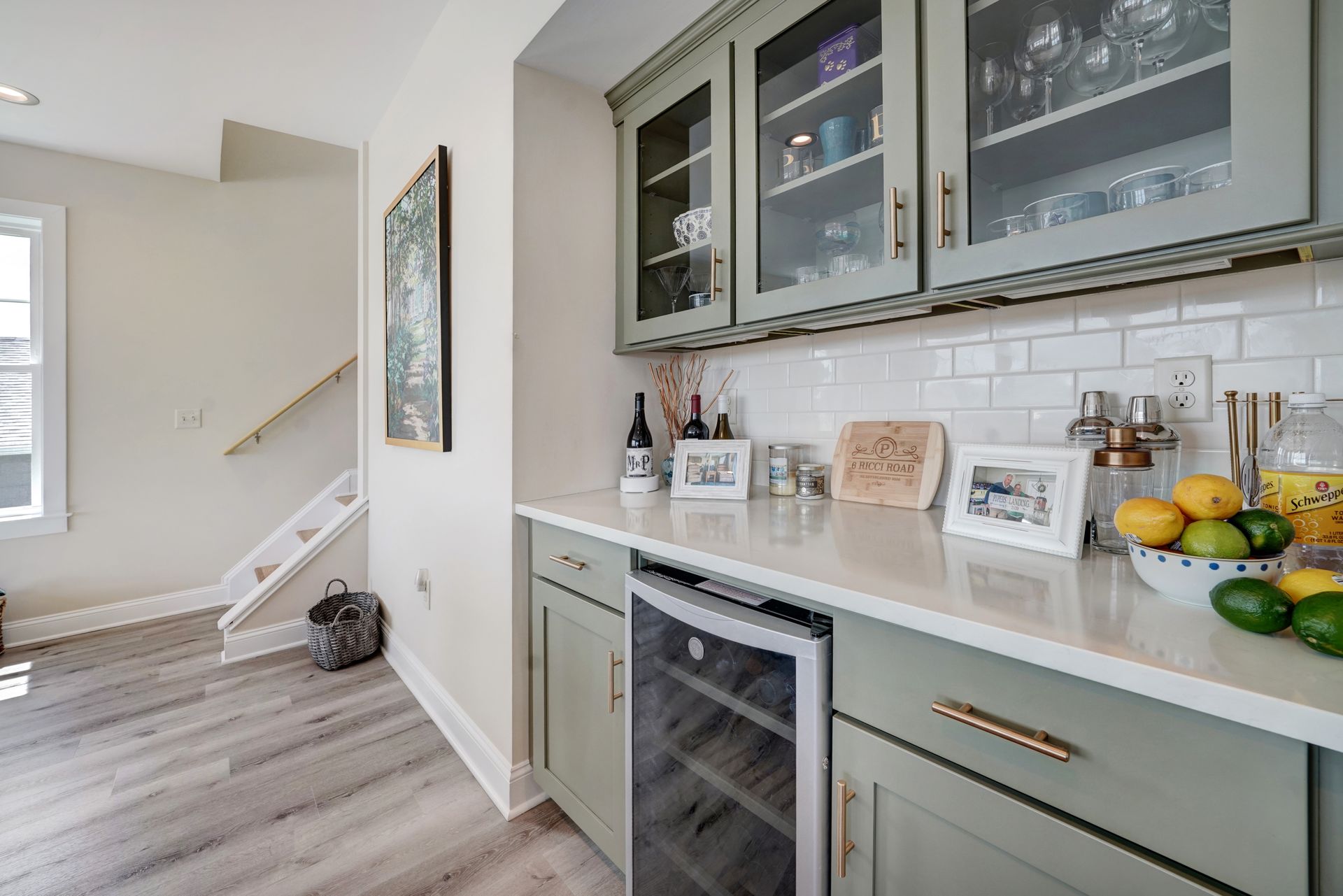 Kitchen area with green cabinets, white countertop, wine fridge, and glass-fronted cabinets.