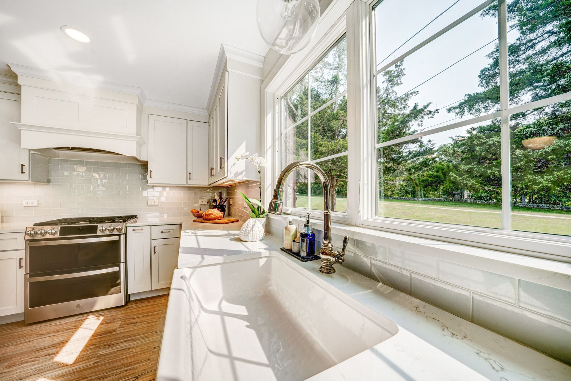 Bright kitchen with white cabinets, large window overlooking greenery, and farmhouse sink.