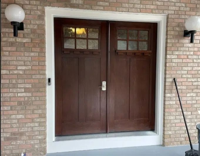 Double brown doors with window panes, flanked by white globe lights on a brick facade.
