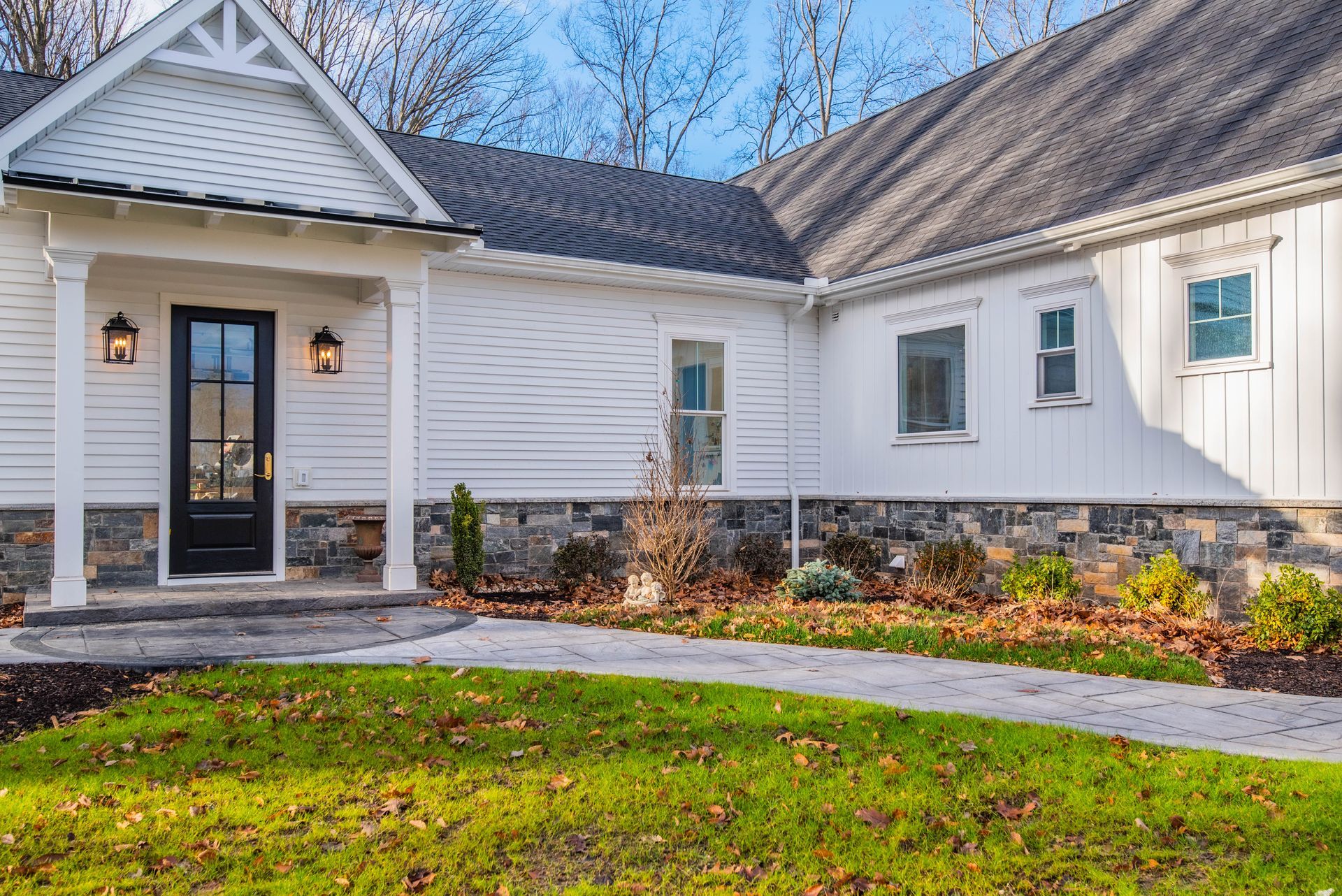 White house with black door, stone accents, and walkway on green lawn.
