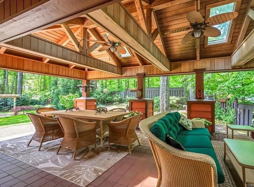 Outdoor dining and seating area with a wooden pergola, table, sofa, and greenery.