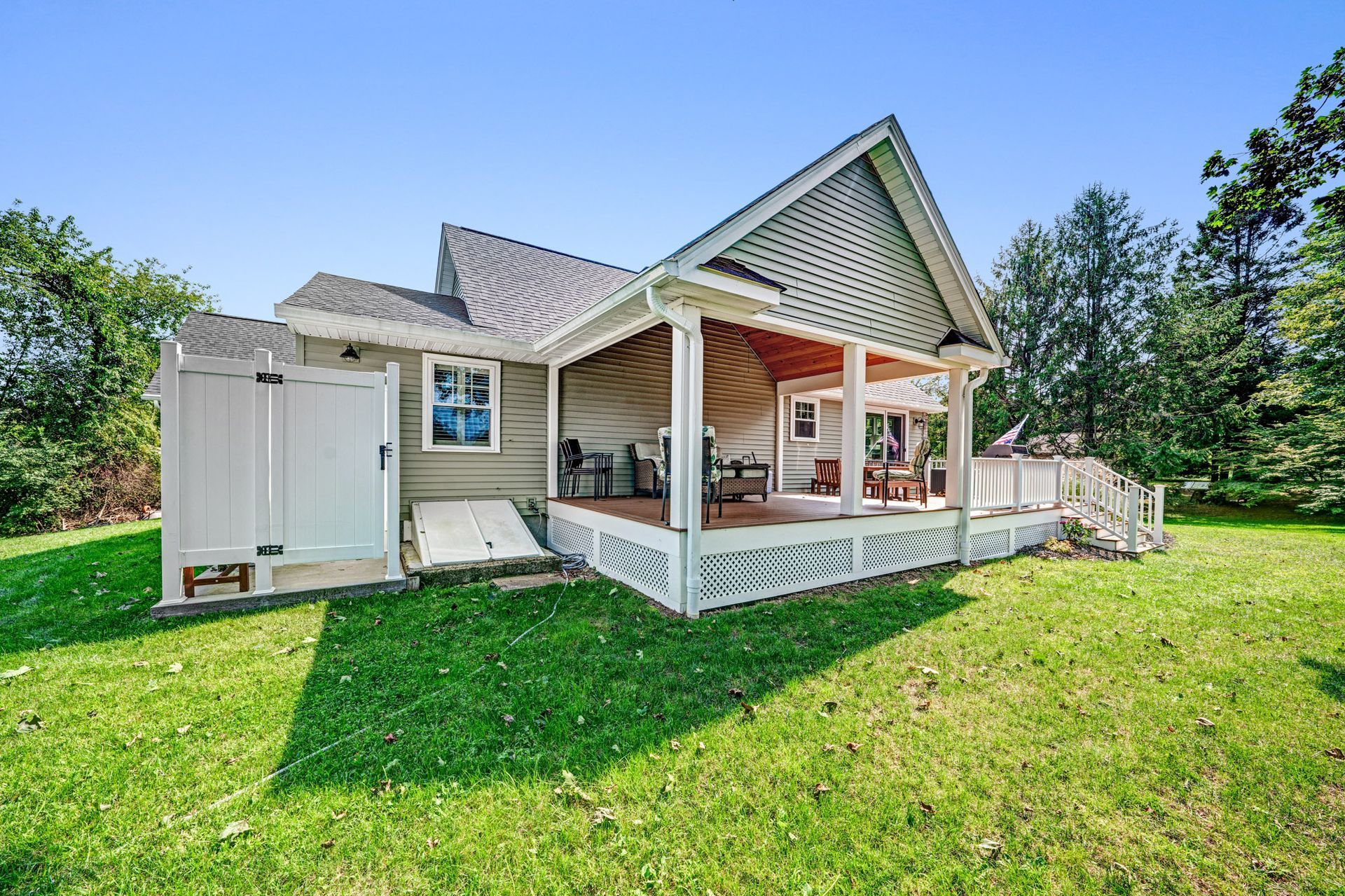 A one-story house with a porch and shed on a grassy lawn under a blue sky.