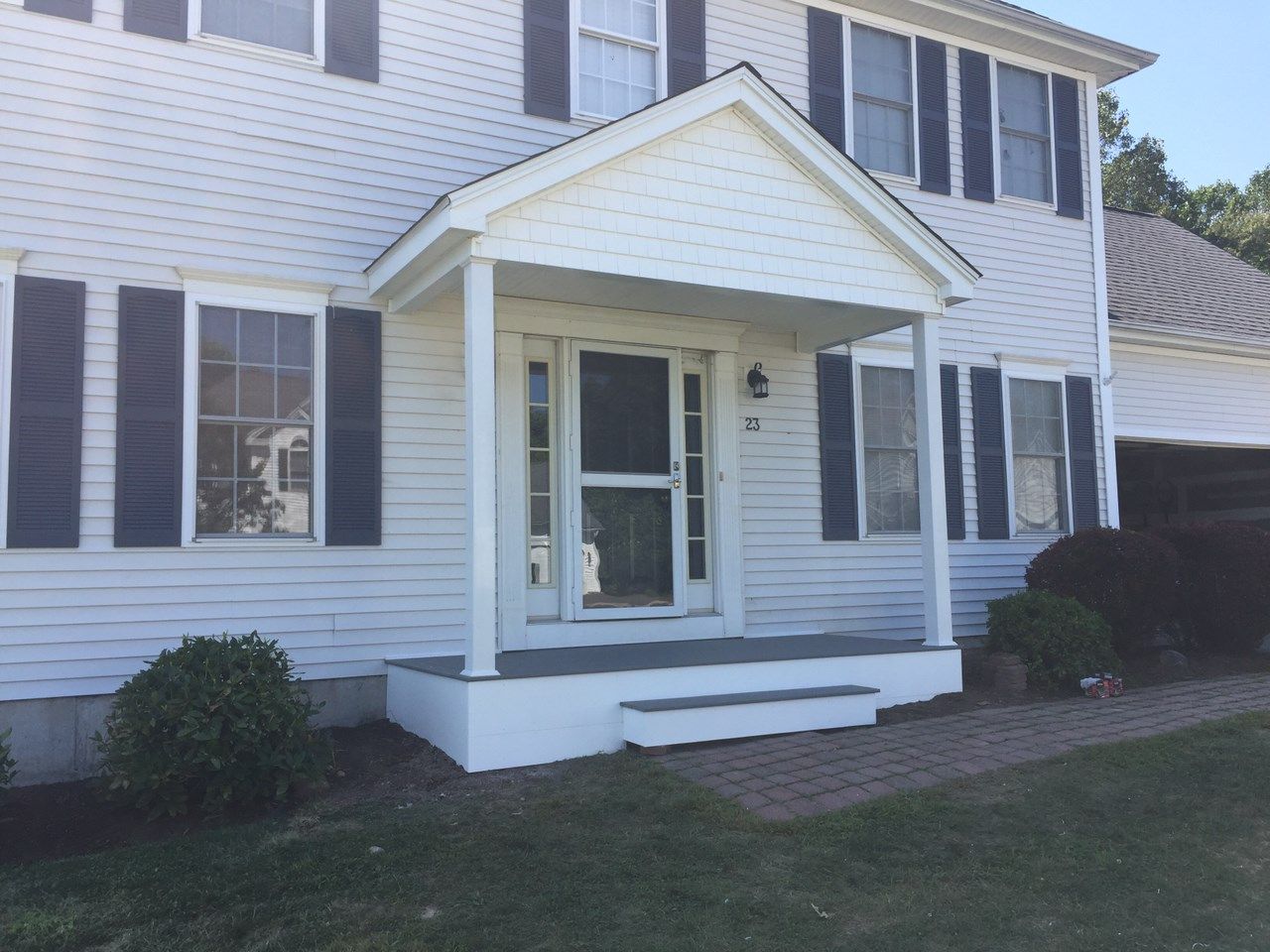 White house with a small porch, blue shutters, and green lawn.