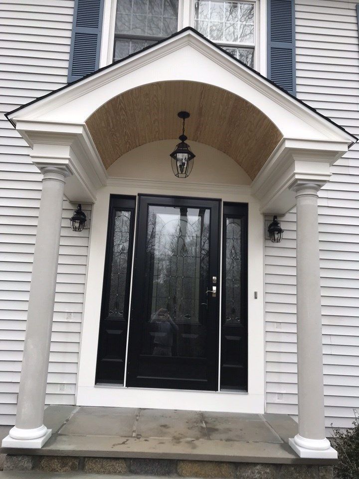 Entrance to a house with black door, sidelights, porch with columns, and blue shutters.