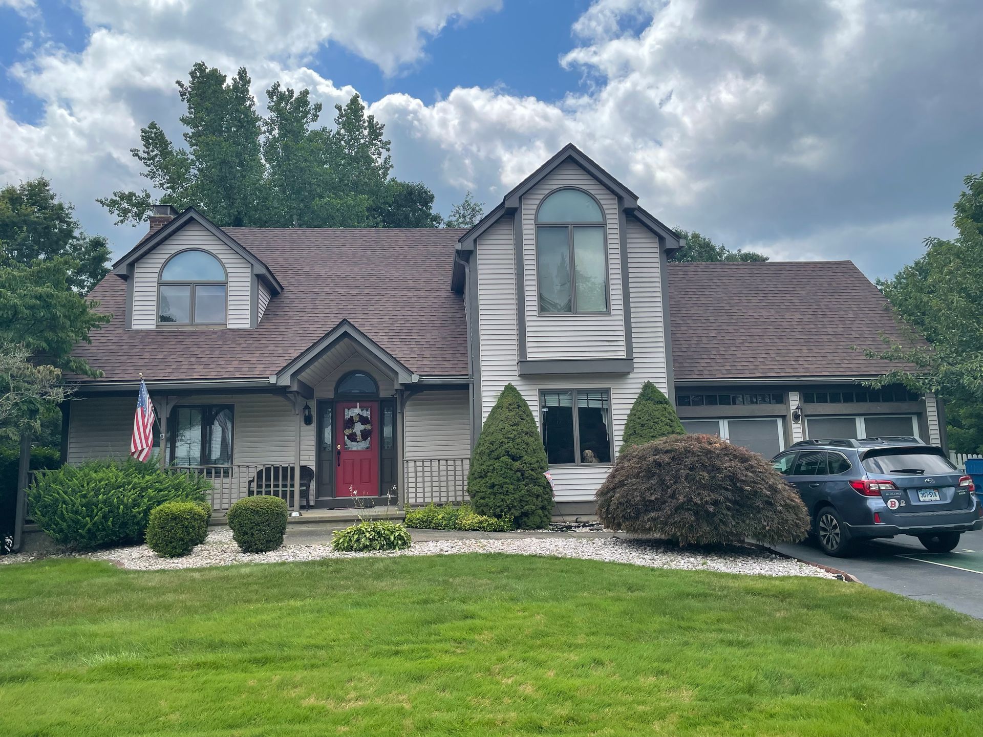 Two-story home with light siding, brown roof, and red front door; parked SUV in the driveway.