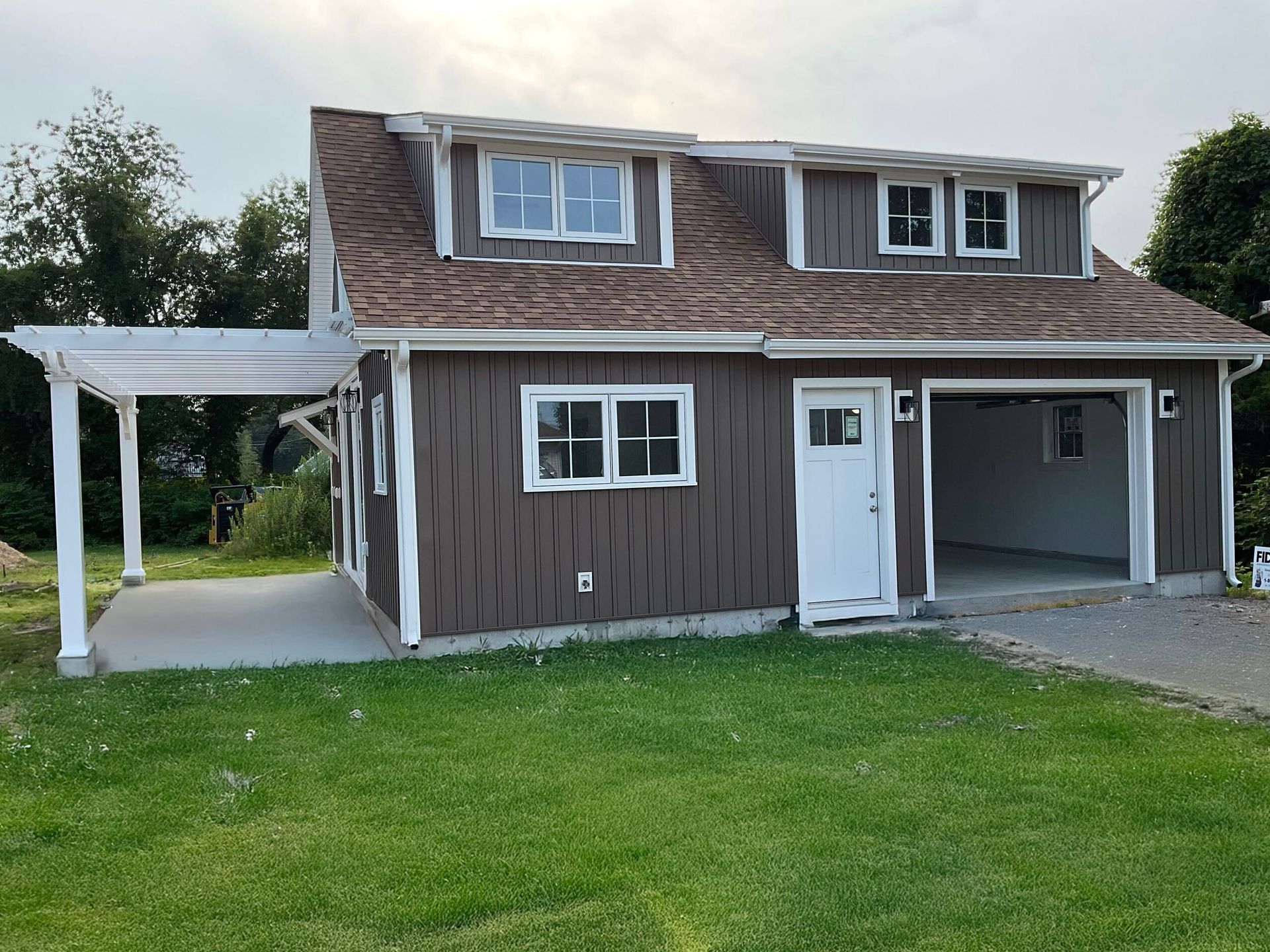 Brown two-story building with a garage, white trim, and a pergola. Green lawn in the foreground.