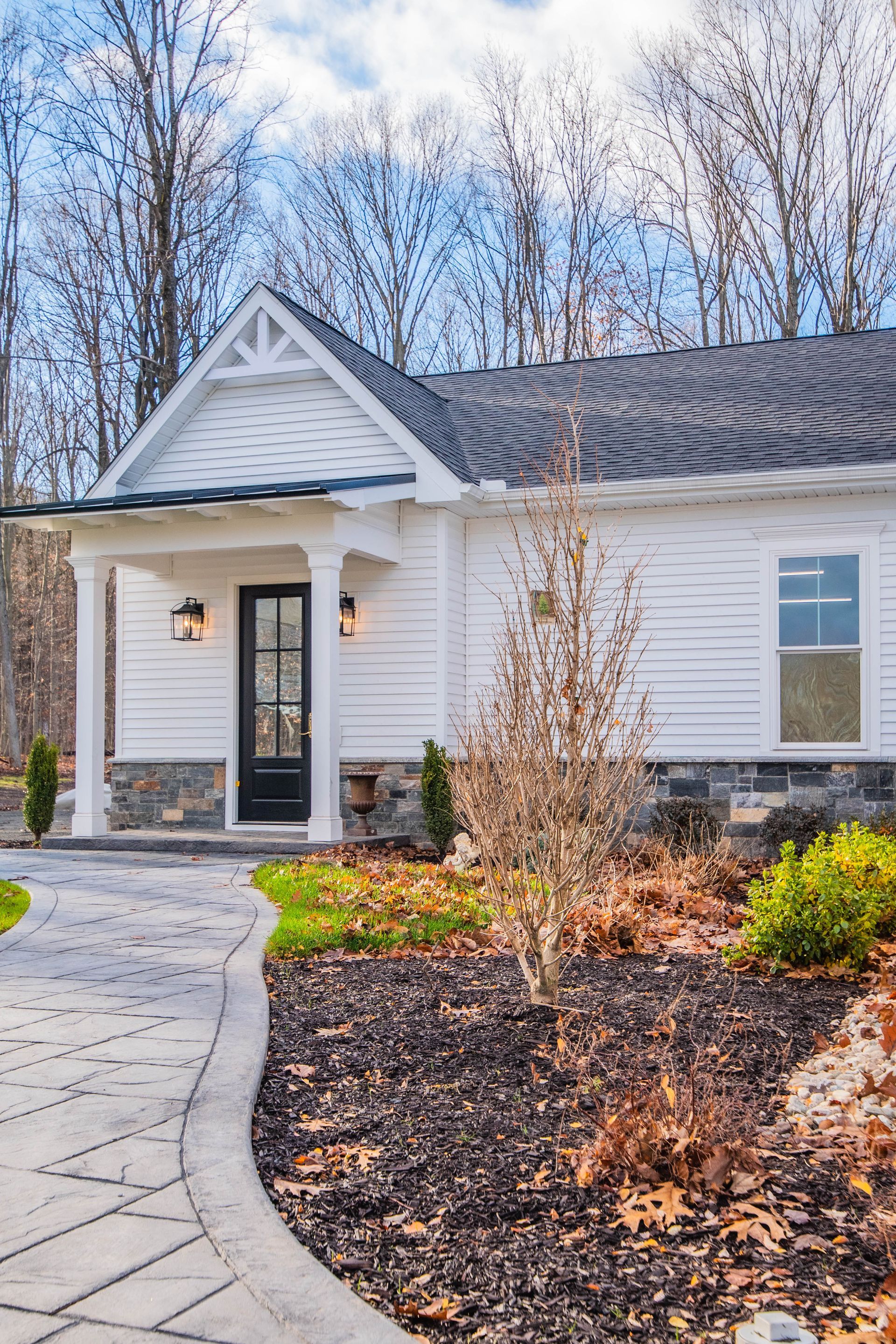 White house with black door, porch, and a stone walkway. Landscaping with bare trees.