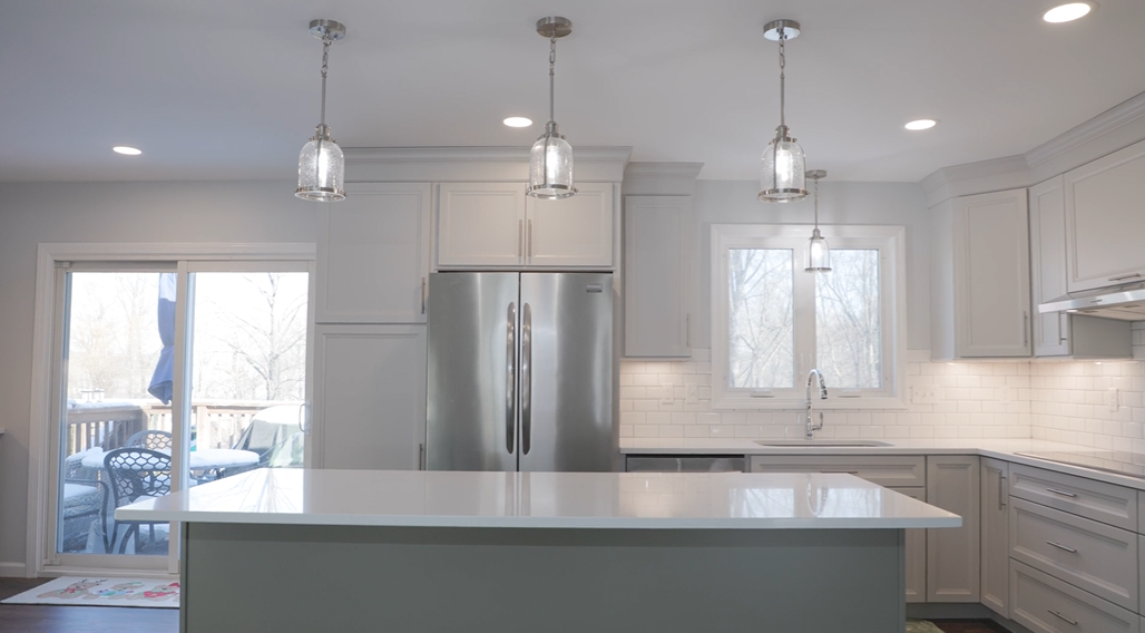 Modern kitchen with white cabinets, stainless steel refrigerator, island, and pendant lights.