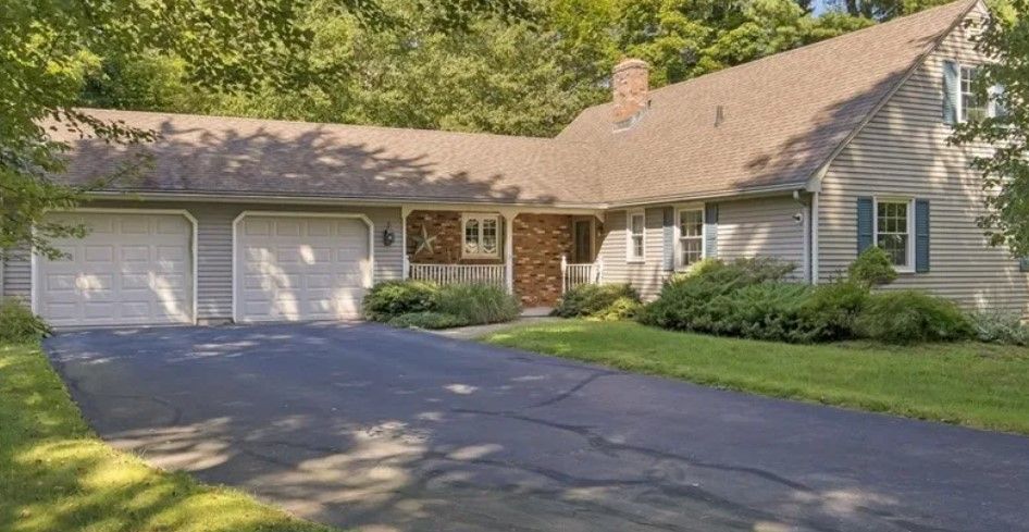 A one-story house with a three-car garage, asphalt driveway, and green lawn.
