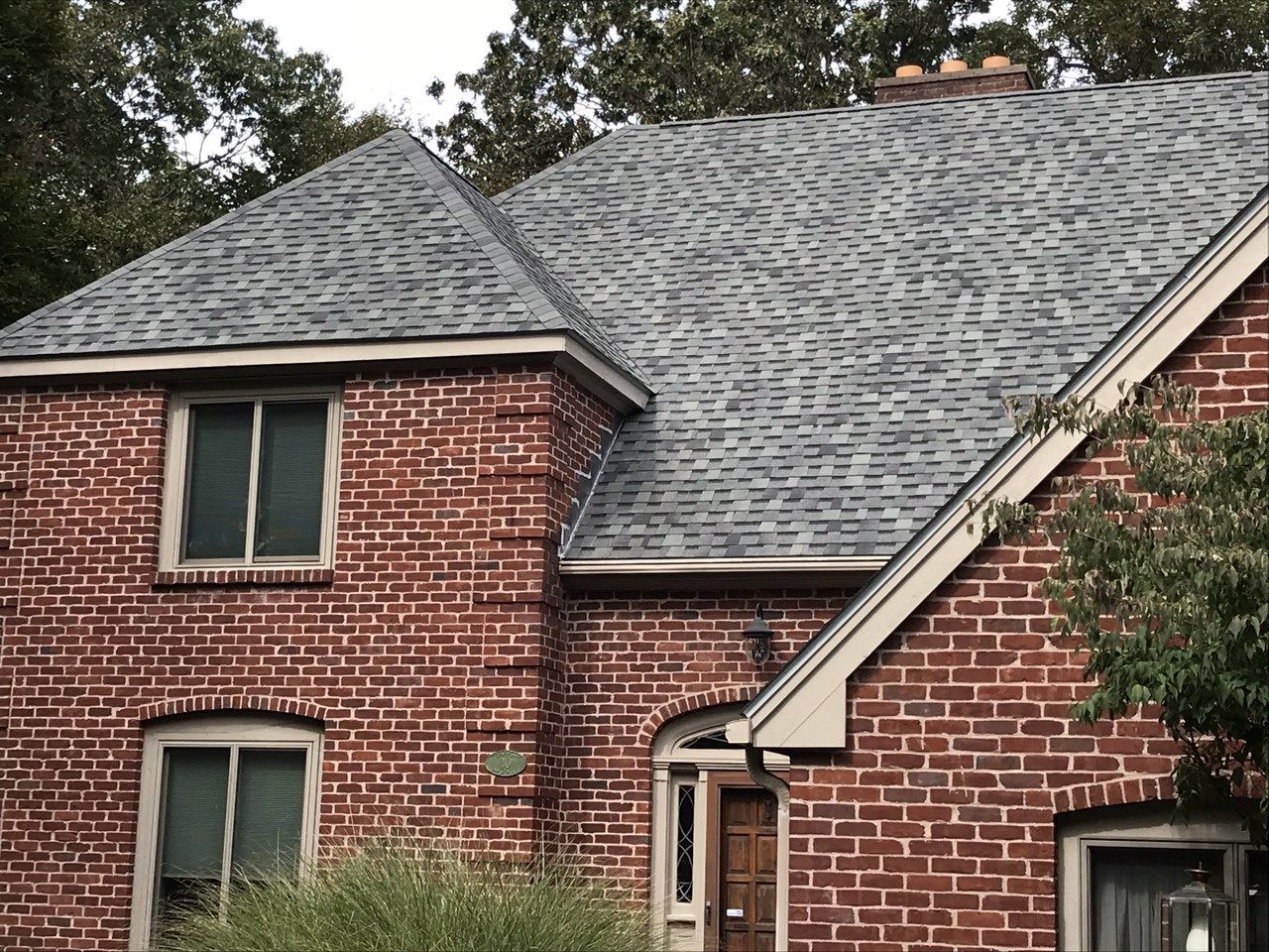 Brick house with grey shingle roof, chimney, and dormer.