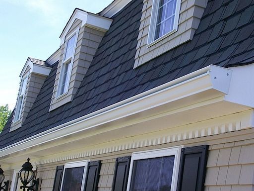 Tan house with dark roof and dormer windows, white trim and gutters.
